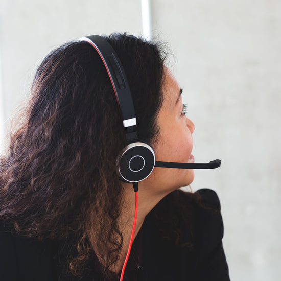 Person wearing a headset with a microphone, standing against a light-colored wall.