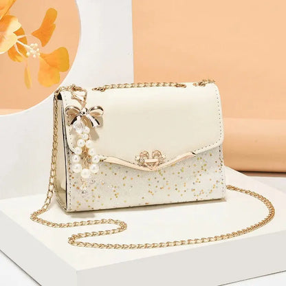 White handbag with gold chain and pearl details on a white and beige background